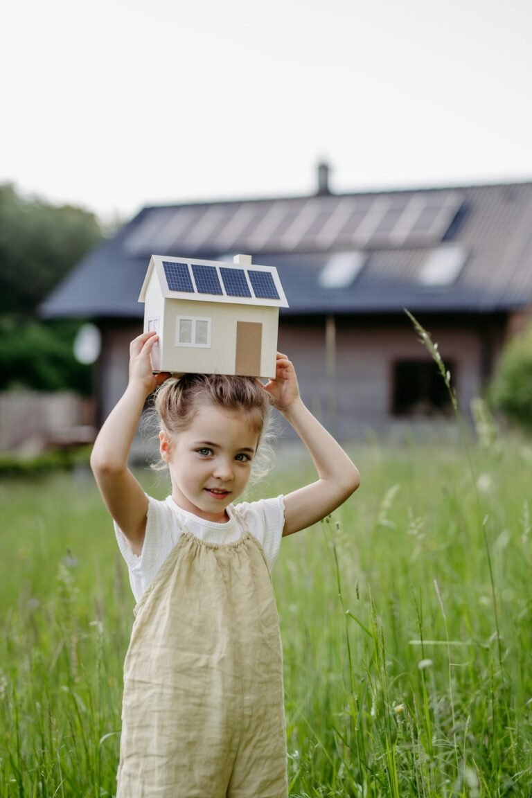 Portraitof little girl holding model of house with solar panels, concept of sustainable lifestyle